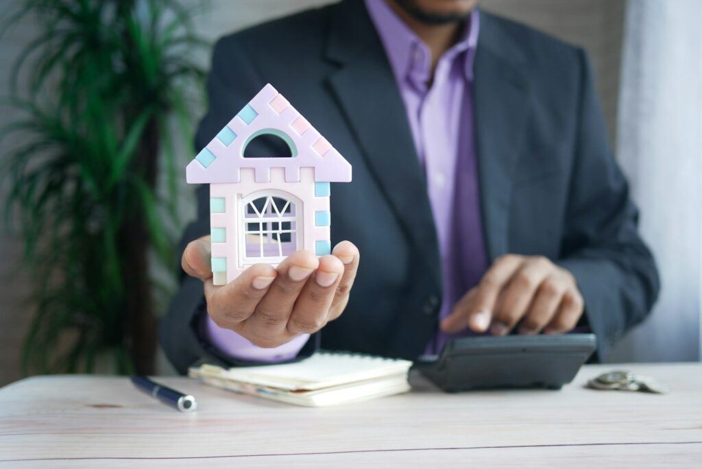 man holding model house at desk with calculator; CLO ratings providers
