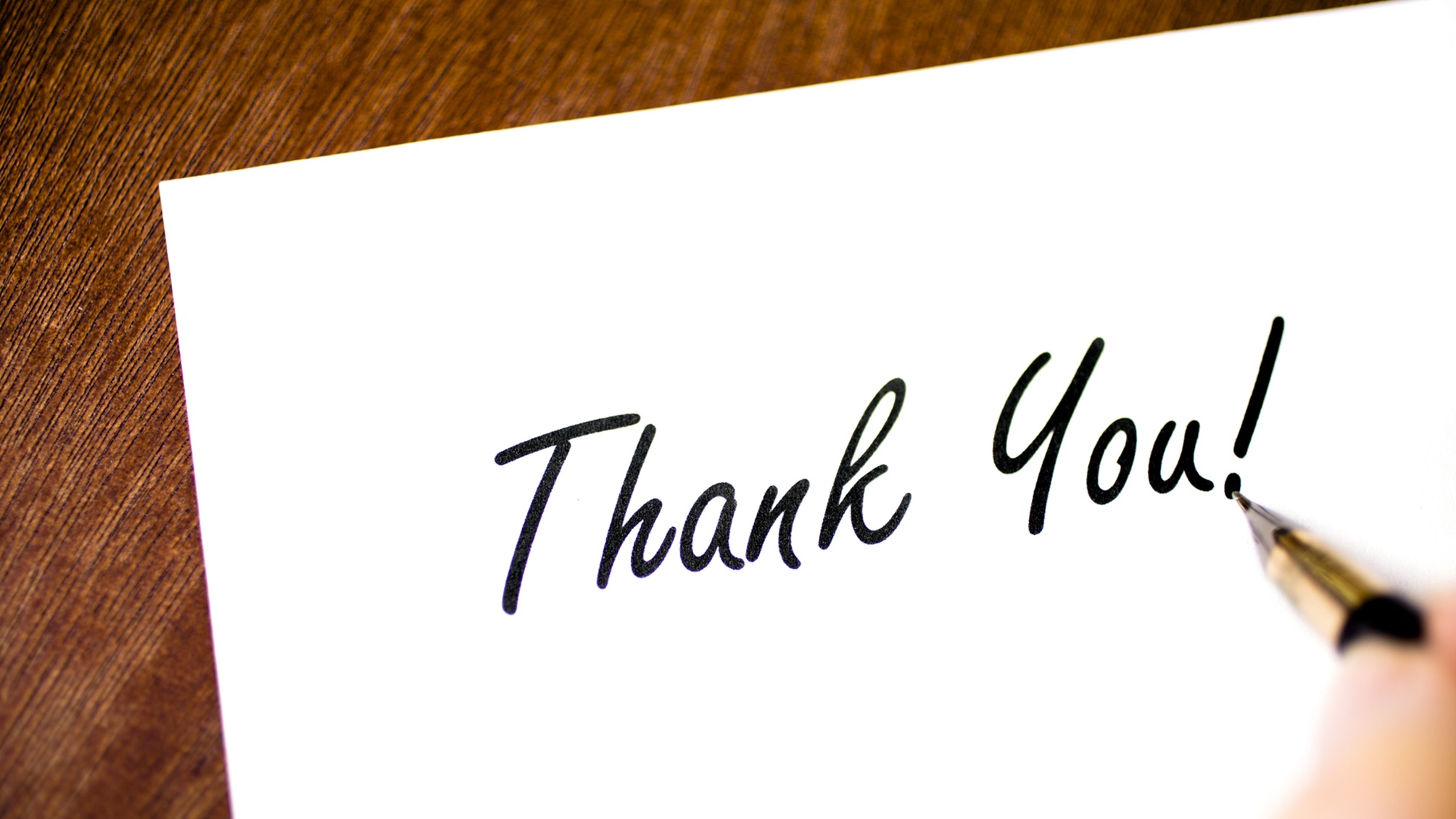 A fountain pen writing the words "thank you," only the writer's fingers showing.