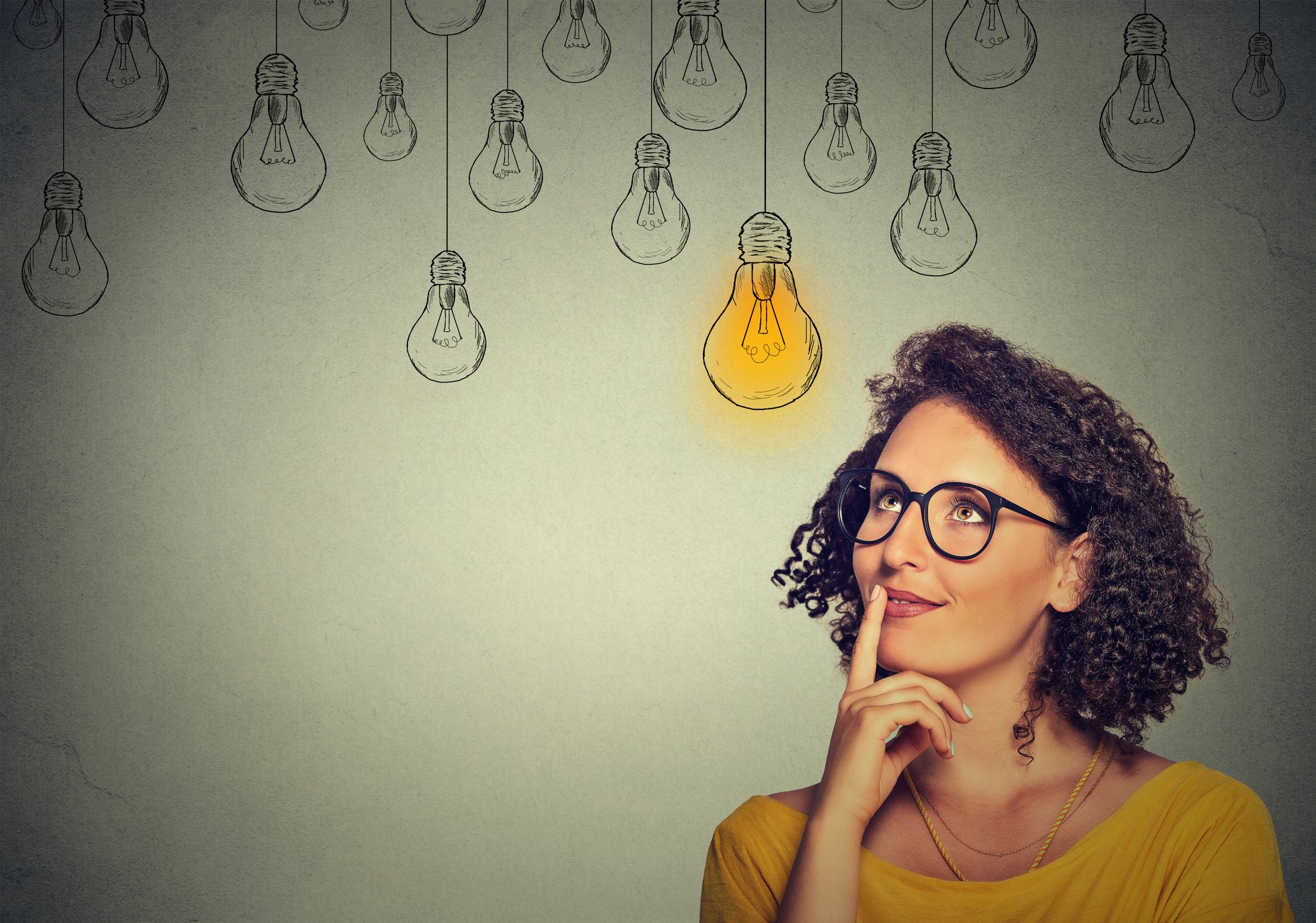 A person looking up at a light bulb with a finger on their lips and thinking. 