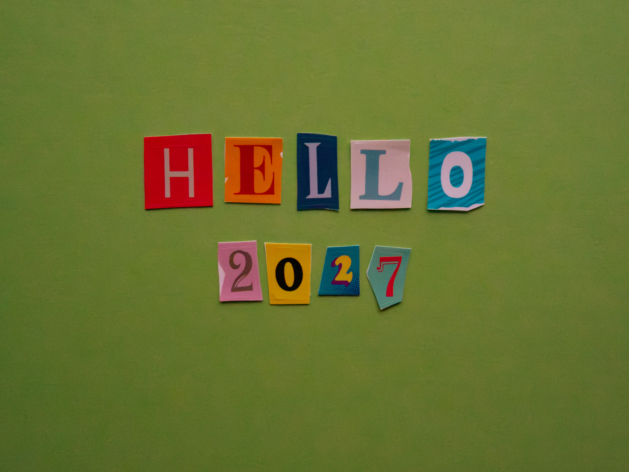 Creative &ldquo;HELLO 2027&rdquo; message made with colorful magazine-style cutout letters and numbers on a green background.