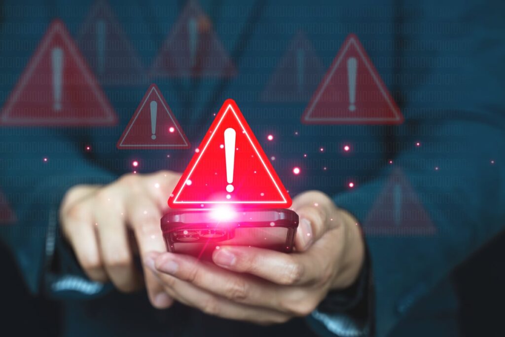 A person holding a smartphone with red triangles containing exclamation points appearing above the phone.