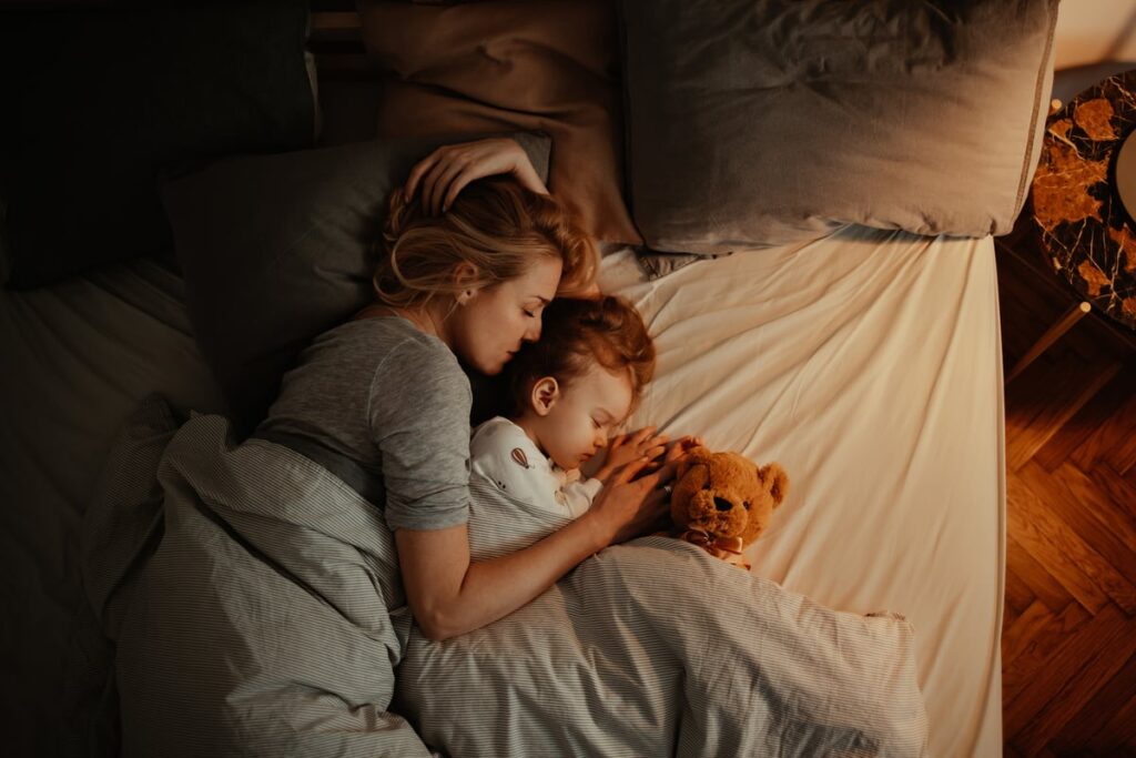Parent, child, and stuffed animal lying in bed.